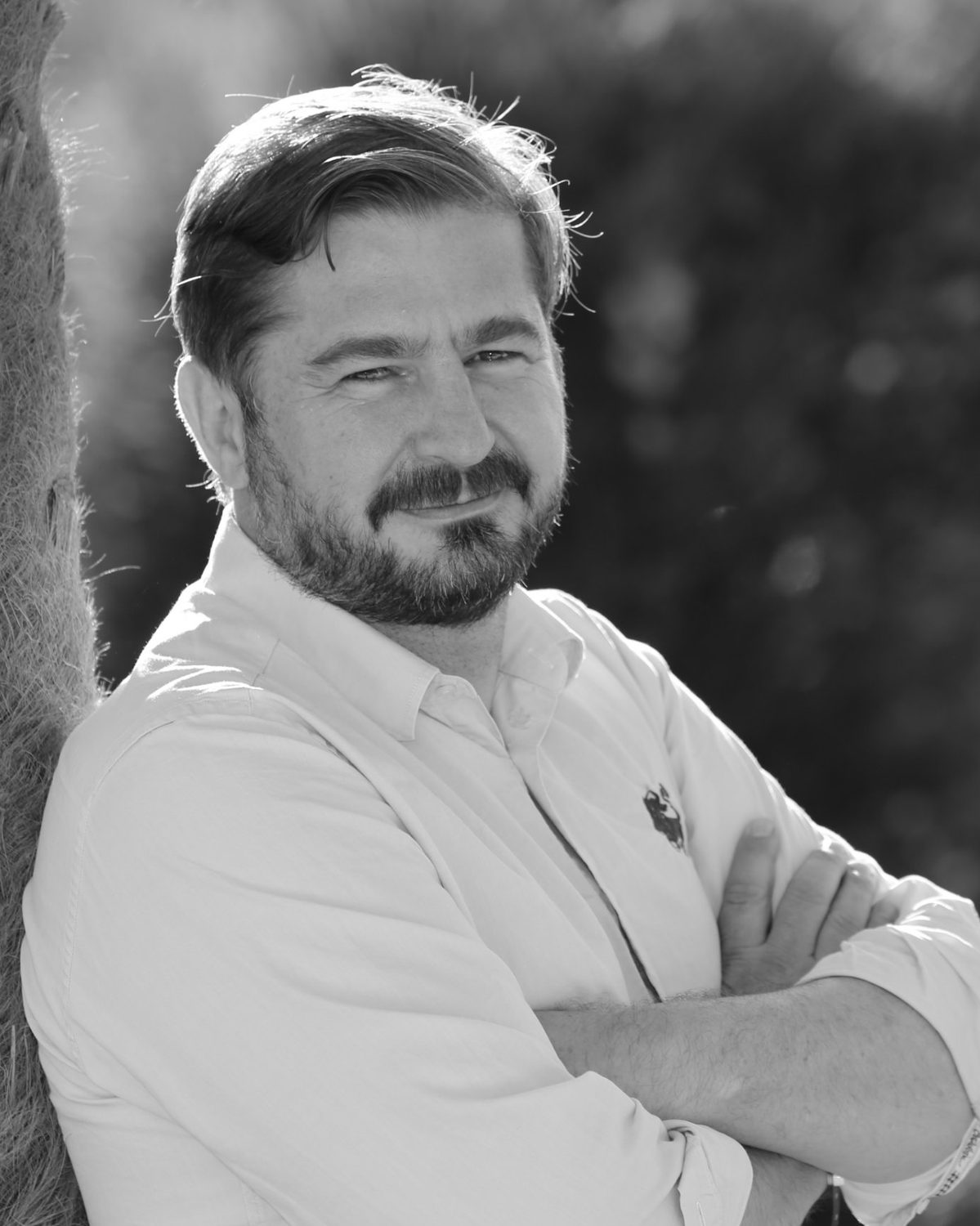 Portrait de Cédric Louard, bras croisés, adossé à un palmier