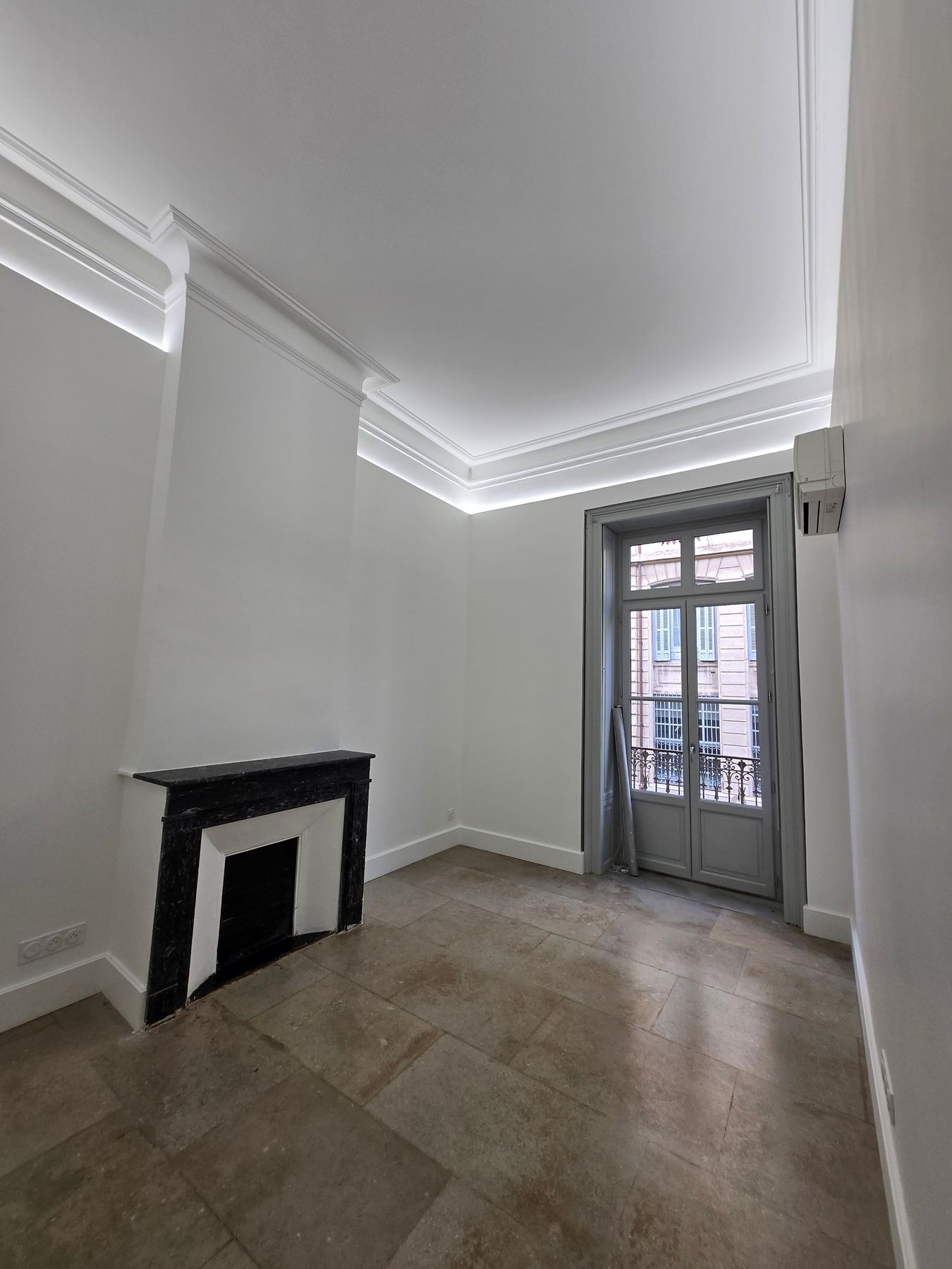Restored room with lit cornices, black marble fireplace and French window